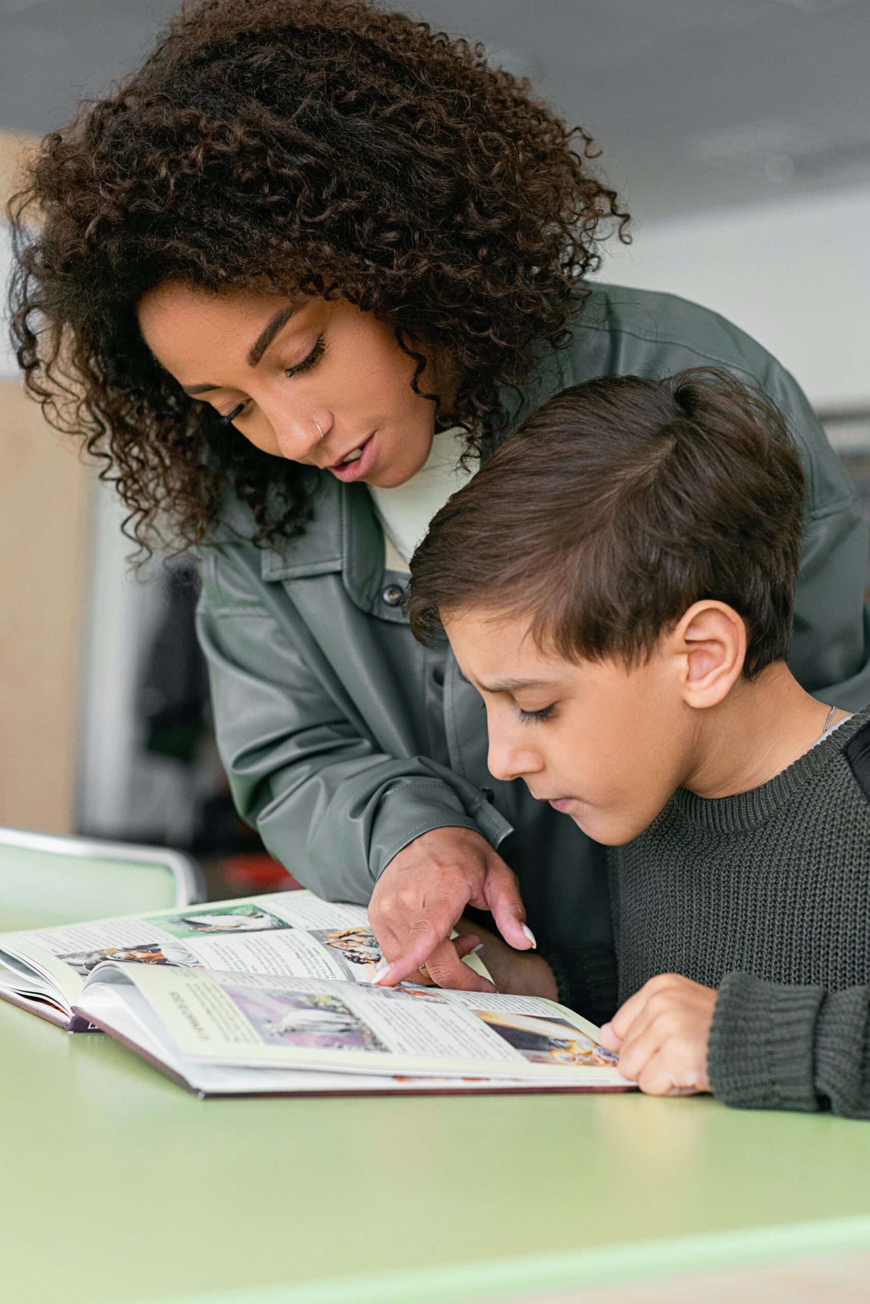 A woman helps a boy read in a classroom setting. Educational support concept.